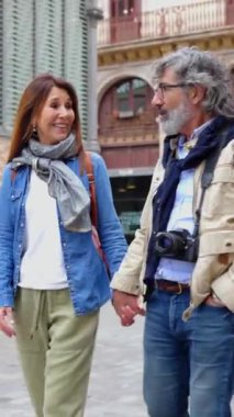 Tatil sırasında Barcelona 'da yürüyüş yaparken gülen mutlu yaşlı çiftlerin dikey HD videosu. Olgun arkadaşlar, birlikte şehir sokaklarında eğleniyorlar.