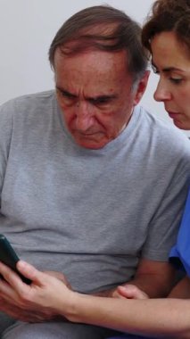 Dikey video. Ev ziyareti sırasında hastasına cep telefonunu nasıl kullanacağını öğreten dost canlısı bir bakıcı. Yaşlılar yaşam tarzı ve teknoloji kavramı