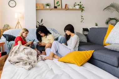 Üç bayan arkadaş evde pijama partisi sırasında akıllı telefonlarını kullanarak oturma odasında dinleniyorlar. Kadın arkadaşlığı ve gençlik kavramı