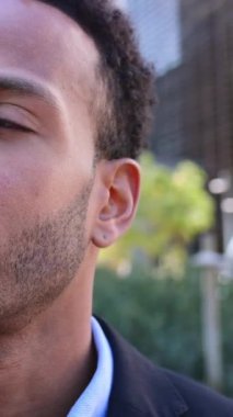 Kendine güvenen Afro-Amerikan iş adamının yakın plan portresi dışarıda ofis binasının yanında duran kameraya bakıyor. Çekici, profesyonel bir erkeğin vesikalığı. Dikey HD video
