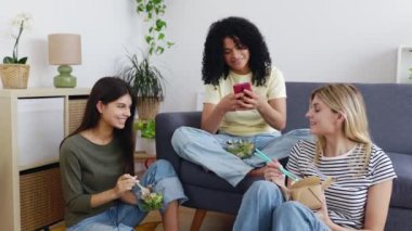 Milenyum çeşitliliği olan kadınlar akıllı telefon uygulamasında sosyal medya içeriğine bakarken gülüyorlar. Bir grup genç bayan arkadaş evde birlikte vakit geçiriyorlar. Teknoloji ve ev hayatı