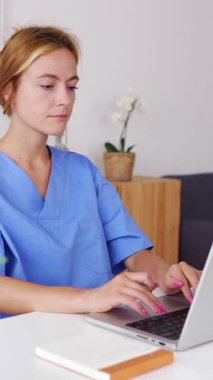 Mavi üniformalı güzel bir sağlık çalışanının eve vardıktan sonra not defterine not alarak çalıştığı dikey bir video. Hastane tıbbi yaşam tarzı konsepti