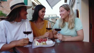 Restoran masasının önünde oturmuş kırmızı şarapla aperatifin tadını çıkaran üç tane çok ırklı genç kadın. Kadın arkadaşlığı ve tatil yaşam tarzı konsepti.