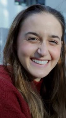 Üniversite kampüsünde arkadaşlarıyla birlikte okuyan mutlu genç bir kızın dikey video portresi. O, dişlek gülümseme gösteren kameraya gülümsüyor