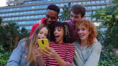 Genç Gen Z grubu, şehirdeki şehir merdivenlerinde birlikte oturan cep telefonu uygulamasında sosyal medya içeriğini izlerken eğleniyor. Gençlik yaşam tarzı ve teknoloji kavramı