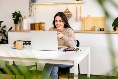 Evden uzaktan ders çalışan gülümseyen genç bir üniversite öğrencisi. Mutfağındaki dizüstü bilgisayarında bir video kaydı var. Eğitim yaşam tarzı kavramı
