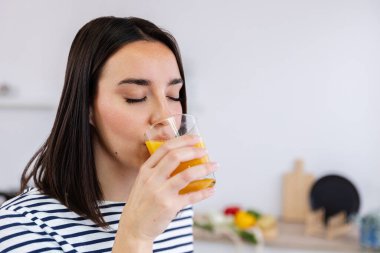 Genç ve güzel bir kadının sabahın köründe evdeki mutfakta portakal suyu içtiği dikey bir fotoğraf. Sağlıklı yaşam tarzı kavramı