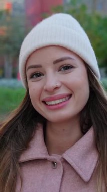 Şehir caddesinde kameraya gülümseyen kışlık elbiseli güzel bir kadının dikey portresi. Beyaz tenli çekici kız dışarıda gülümsüyor. Gençlik kavramı.