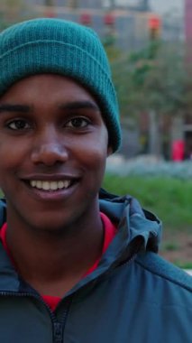 Dikey video. Kış şehrinde kameraya gülümseyen, sıcak kıyafetler giyen, kendine güven ve mutluluk saçan mutlu genç Afrikalı Amerikalı adam. Gen Z 'nin portresi Şehir Caddesinde zenci çocuk