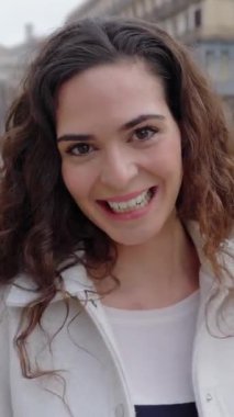 Dikey HD video görüntülerinde gülümseyen yetişkin bir kadın kameraya bakıyor. Şehir caddesinde kendini pozitif hissediyordu.