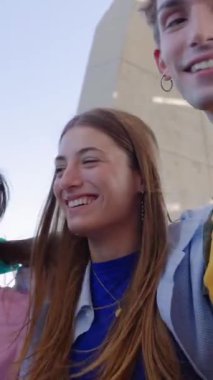 Dikey video. Çeşitli gençler birlikte eğleniyor. Açık havada birbirlerini kucaklıyorlar. Öğrenci genç arkadaşlar dışarıda takılırken gülüyorlar. Gençlik toplumu kavramı.