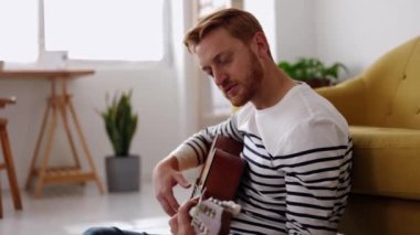 Genç hippi adam açık salonda dinlenirken gitar çalıyor. Boş zaman ve müzik konsepti