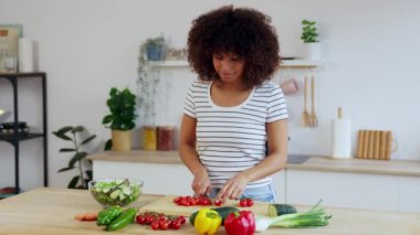 Genç, mutlu bir kadın parlak mutfakta domates dilimliyor, yeşil salatayı domates, soğan ve biberle hazırlıyor. Sağlıklı yaşam tarzı ve gıda konsepti
