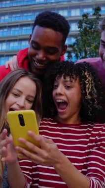Genç Gen Z grubunun şehirdeki kentsel merdivenlerde birlikte oturan cep telefonu uygulamasında sosyal medya içeriğini izlerken eğlendiği dikey HD videoları. Gençlik yaşam tarzı konsepti