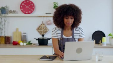 Mutfakta yemek yaparken dizüstü bilgisayarda çalışan genç ve mutlu bir kadın. Seyahat ve iş konsepti