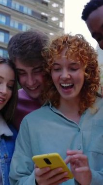 Cep telefonu uygulamasından komik içerikler izleyen çok ırklı gençlerin dikey videosu. Milenyum çeşitliliği olan arkadaşlar dışarıda akıllı telefon cihazları kullanarak eğleniyorlar. Gençlik ve teknoloji kavramı