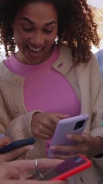 Dikey video. Çok ırklı bir grup genç arkadaş şehirde dikilen cep telefonlarından sosyal medya içeriğini izlerken eğleniyor. Milenyum insanları akıllı telefon uygulamasında eğlenceli videolar izliyorlar.