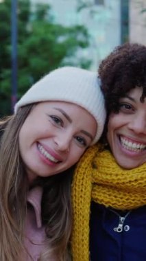 Dikey video. Üç farklı kadın arkadaş, soğuk bir kış gününde birbirlerine mutlu bir şekilde poz veriyorlar sıcak ve sıcak giysiler içinde birbirlerine sarılıyorlar. Kadın arkadaşlığı kavramı
