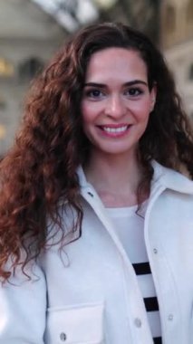 Tren istasyonunda kameraya gülümseyen genç bir kadının dikey HD videosu. Seyahat ve tatil kavramı.