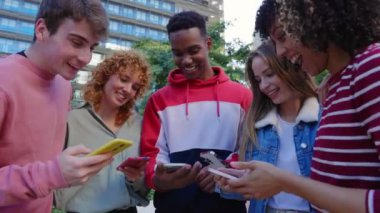 Dışarıda cep telefonuyla eğlenen bir grup genç öğrenci. Cep telefonu uygulamasından sosyal medya içeriğini izleyen çok ırklı arkadaşlar. Gençlik ve teknoloji eğilimleri kavramı