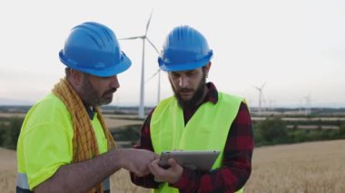 İki mühendis dijital tablet kullanarak rüzgar türbinlerinin bakımını tartışıyor. Yenilenebilir ve alternatif enerji kavramı
