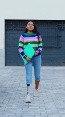 Protez bacaklı genç bir kızın üniversite kampüsünde arkadaşlarıyla buluşmasının dikey HD videosu. Eğitim, çeşitlilik ve gençlik toplumu kavramı. Yapay uzuv.