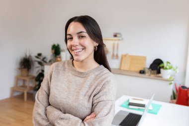 Parlak ve havadar bir mutfakta kollarını kavuşturarak gülümseyen kendinden emin genç bir kadın uzaktan çalışırken pozitiflik ve motivasyon yayıyor.