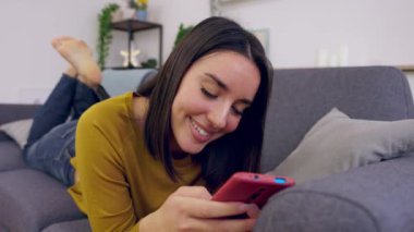 Genç, mutlu, güzel bir kadın evdeki koltukta uzanmış arkadaşlarıyla sohbet ediyor ya da internette geziniyor, sosyal medya içeriğinden keyif alıyor. Teknoloji yaşam tarzı konsepti