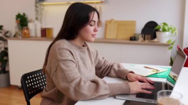 Genç mutlu genç kız evdeki mutfakta dizüstü bilgisayar kullanarak internetten ders çalışıyor. E-öğrenim ve eğitim yaşam tarzı konsepti.