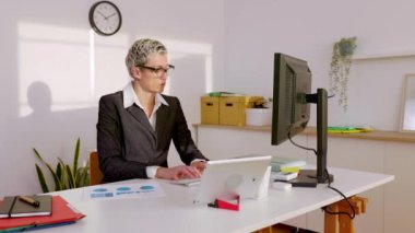 Başarılı bir orta yaşlı kadın serbest çalışan, kendi ofisinden çalışan, kablosuz bir klavye kullanan ve bilgisayar ekranına bakan. İş, iletişim ve serbest insan kavramı