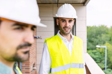Güvenlik teçhizatı kullanan iki mühendis, karmaşık planlara odaklanmış yoğun bir inşaat sahasında işbirliği yapıyorlar. Mühendislik ve mimari kavramı