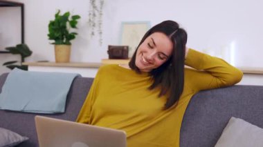 Mutlu genç, güzel bir kadın evdeki kanepede otururken dizüstü bilgisayarında bir video görüşmesi yapıyor. Sosyal uzaklık ve çevrimiçi iletişim kavramı.