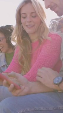 Dışarıda cep telefonu kullanarak eğlenen bir grup mutlu öğrencinin dikey HD videosu. Gülümseyen çok ırklı arkadaşlar cep telefonu uygulamasından sosyal medya içeriğini izliyorlar. Gen teknoloji insanları konsepti