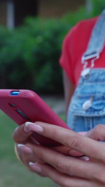 Dikey HD video. Şehir caddesinde akıllı cep telefonu kullanan tanınmayan genç bir bayanı kapatın. Milenyum kızı dışarıda akıllı telefondan konuşuyor. Kırmızı renk.