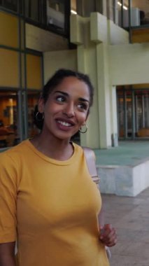 Genç Amerikalı kız öğrencinin üniversite kampüsündeki meslektaşlarıyla konuştuğu dikey HD video. Latin sınıf arkadaşları okuldan sonra lisenin önünde sosyalleşiyor.