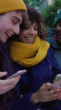 Şehir bankında oturan genç arkadaşların cep telefonlarını kullandıkları dikey HD videolar. Çok ırklı bin yıllık öğrenci, sıcak kıyafetler içinde sosyal medyada geziniyor ve internete bağlanıyor.