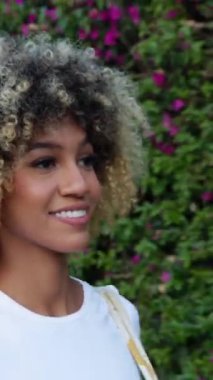 Genç ve güzel Latin Amerikalı bir kadının şehir sokaklarında yürüdüğü dikey HD video. Neşeli milenyum melez kadınlar yazın açık havada yürüyüş yapıyorlar. İnsanlar ve mutluluk kavramı.