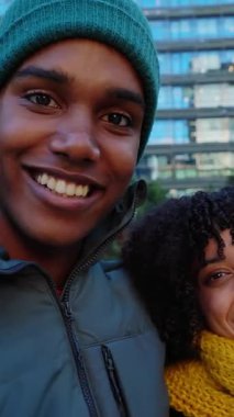 Sıcak kıyafetler içindeki mutlu gençlerin, kışın City Caddesi 'nde birbirlerine gülümseyen dikey HD video portresi. Milenyum çeşitliliği olan arkadaşlar açık havada birlikte dinleniyorlar.