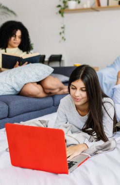 Arkadaşları bir pijama partisi sırasında arka planda kitap okurken genç kız dizüstü bilgisayar kullanarak yatakta uzanıyor. Kadın arkadaşlığı ve gençlik kavramı