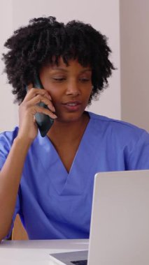 Doktorların ofisinde dizüstü bilgisayarla çalışırken cep telefonuyla konuşan mutlu Latin Amerikalı bir tıp uzmanının dikey HD videosu. Sağlık ve Tıp Konsepti.