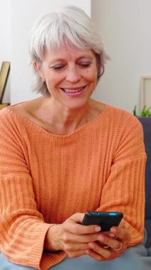 Dikey HD video. Kış gününün tadını çıkarırken cep telefonuyla eğlenen, haber okuyan ya da uygulamadan sosyal medya içeriğini izleyen son sınıf öğrencisi mutlu bir kadın. Teknoloji yaşam tarzı konsepti.