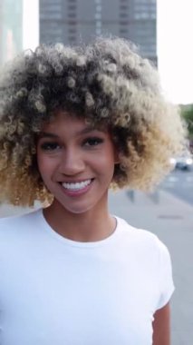 City Street 'te dans eden mutlu Latin Amerikalı kadının dikey HD videosu. Bin yıllık etnik kızın telefondaki dans müziğinin keyfini çıkarırken kameraya gülümseyişinin yavaş çekim görüntüsü.