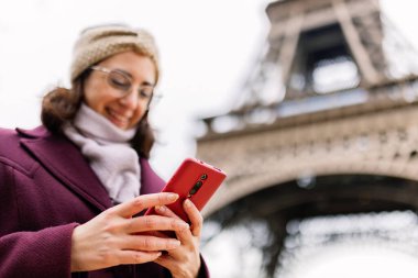 Paris 'teki Eyfel Kulesi yakınlarında cep telefonu kullanan mutlu genç bir kadın. İletişim ve seyahat konsepti. Akıllı telefon aygıtına odaklan