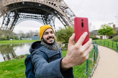 Fransa 'da kış tatili sırasında Paris' te Eyfel Kulesi 'nin önünde fotoğraf çeken sıcak elbiseli mutlu bir adam.