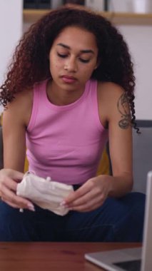 Regl bardağı tutan Latin Amerikalı genç kızın evdeki kanepede oturan dizüstü bilgisayarında kullanma talimatları ararken çekilmiş dikey HD videosu. Kadın hijyen yaşam tarzı konsepti