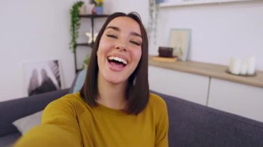 Evdeki kanepede otururken cep telefonuyla video görüşmesi yapan mutlu genç bir kadın. Çevrimiçi iletişim kavramı.