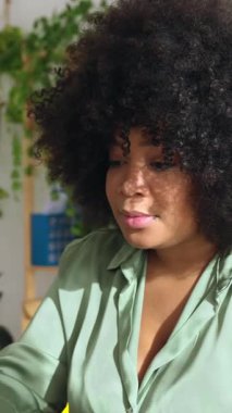 Ofiste dizüstü bilgisayarda çalışan genç Afrikalı Amerikalı kadının dikey HD videosu. Evde bilgisayar kullanan yeşil tişörtlü güzel bir kadın..