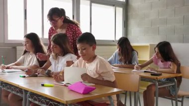 İlkokuldaki sınıfta ilkokul öğrencisine asistanlık yapan genç bayan öğretmen. Eğitim kavramı.