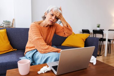 Ateşini ölçen sıcak bir battaniyeye sarılmış, alnına dokunan yaşlı hasta kadın evinde oturma odasından doktorla görüntülü konuşma yapıyor. Sağlık ve tele sağlık kavramı