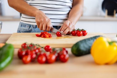 Tahta bir tahtada taze domatesleri dilimleyen bir kadın, çeşitli sebzelerle çevrili, sağlıklı beslenmeyi ve ev yemeklerini somutlaştıran. Sağlıklı yaşam tarzı ve gıda konsepti